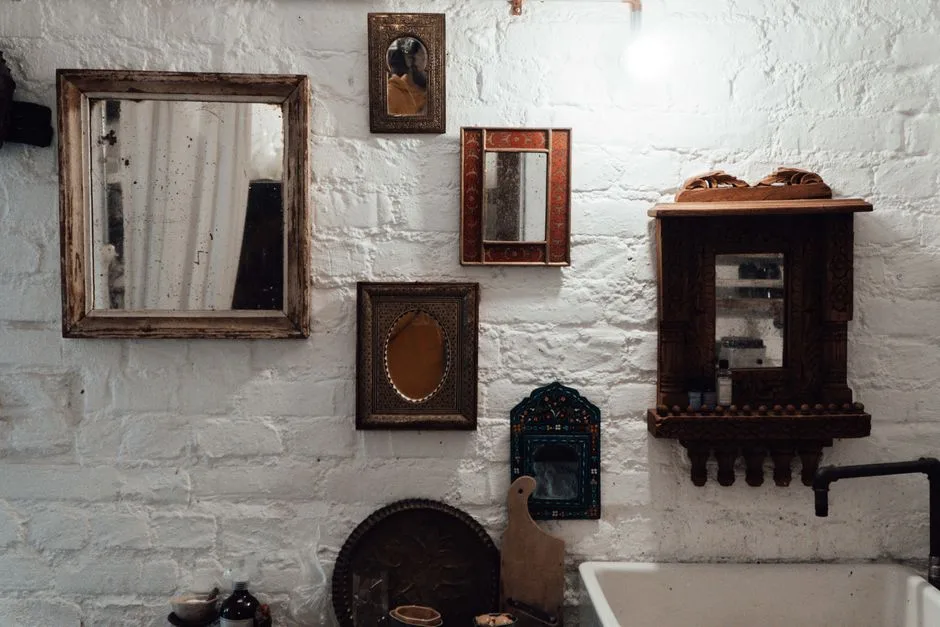 Aged mirrors in decorative frames hanging on rough whitewashed brick wall with shiny light bulb in building