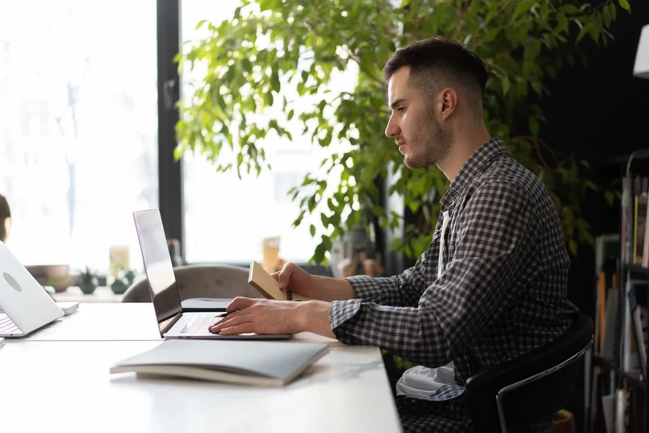 A man working on a laptop in a bright office with natural light and plants, conveying a productive environment.