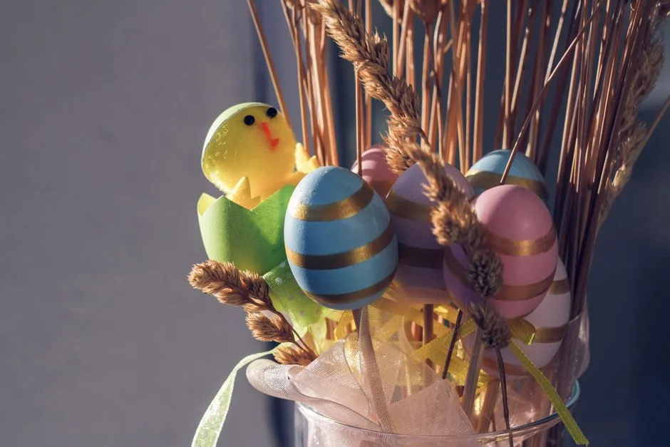 Bunch of bright colored Easter eggs with toy chick and dry branches in glass vase