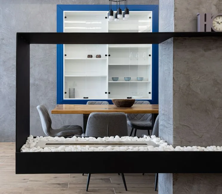 Modern fireplace placed in contemporary apartment near kitchen with chairs at wooden table with bowl and glass cabinet with dishware