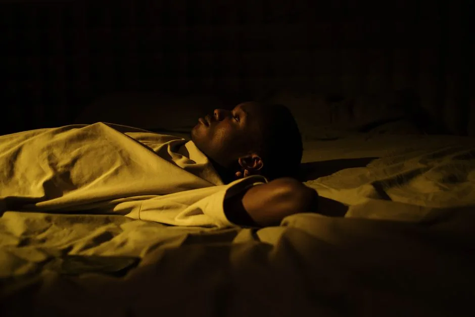 A man struggles with insomnia, lying awake in his dark bedroom at night, reflecting on mental health.