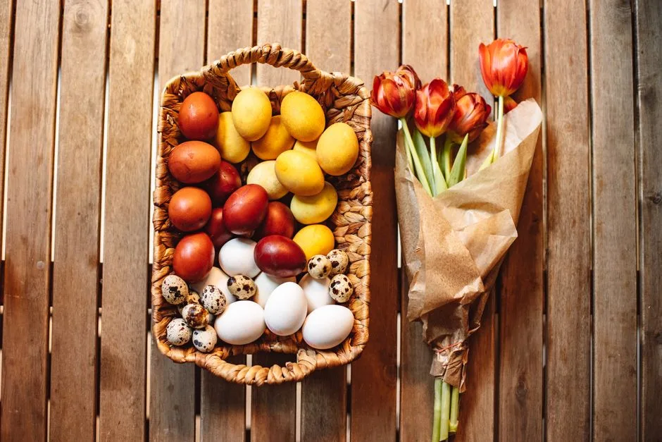 Wicker basket with colorful eggs and bouquet of tulips on wooden surface, perfect for Easter themes.