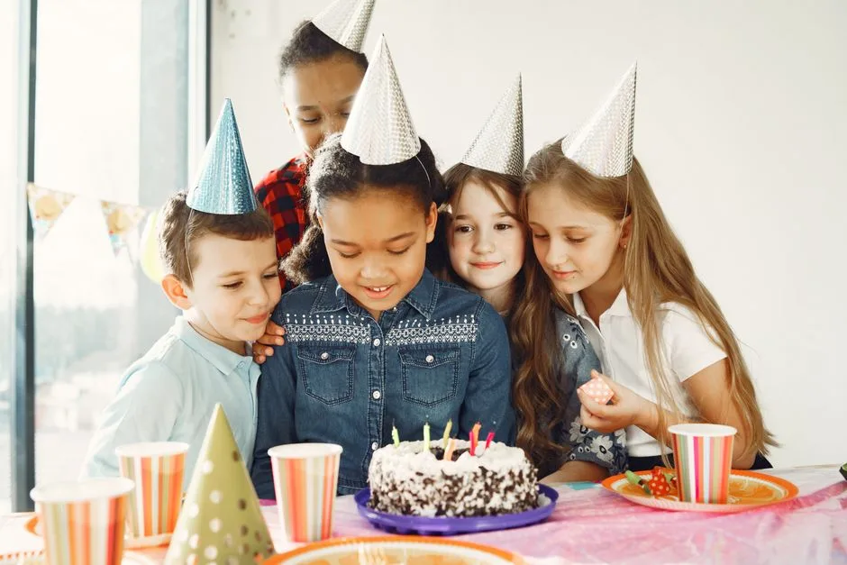 Children gathered around a birthday cake with party hats, celebrating joyfully together.