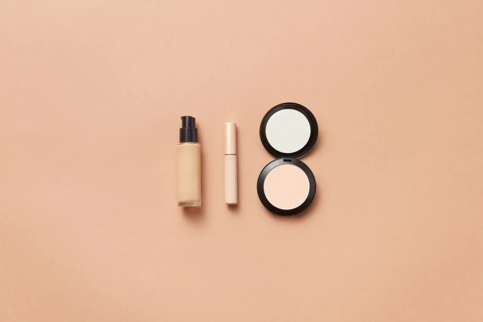 Flatlay of foundation, concealer, and compact powder on beige background. Perfect for beauty and cosmetic themes.