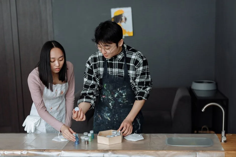 Asian man and woman painting together indoors, exploring creativity.