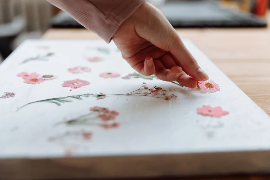 A hand delicately arranging dried pink flowers on a canvas, showcasing creativity in art.