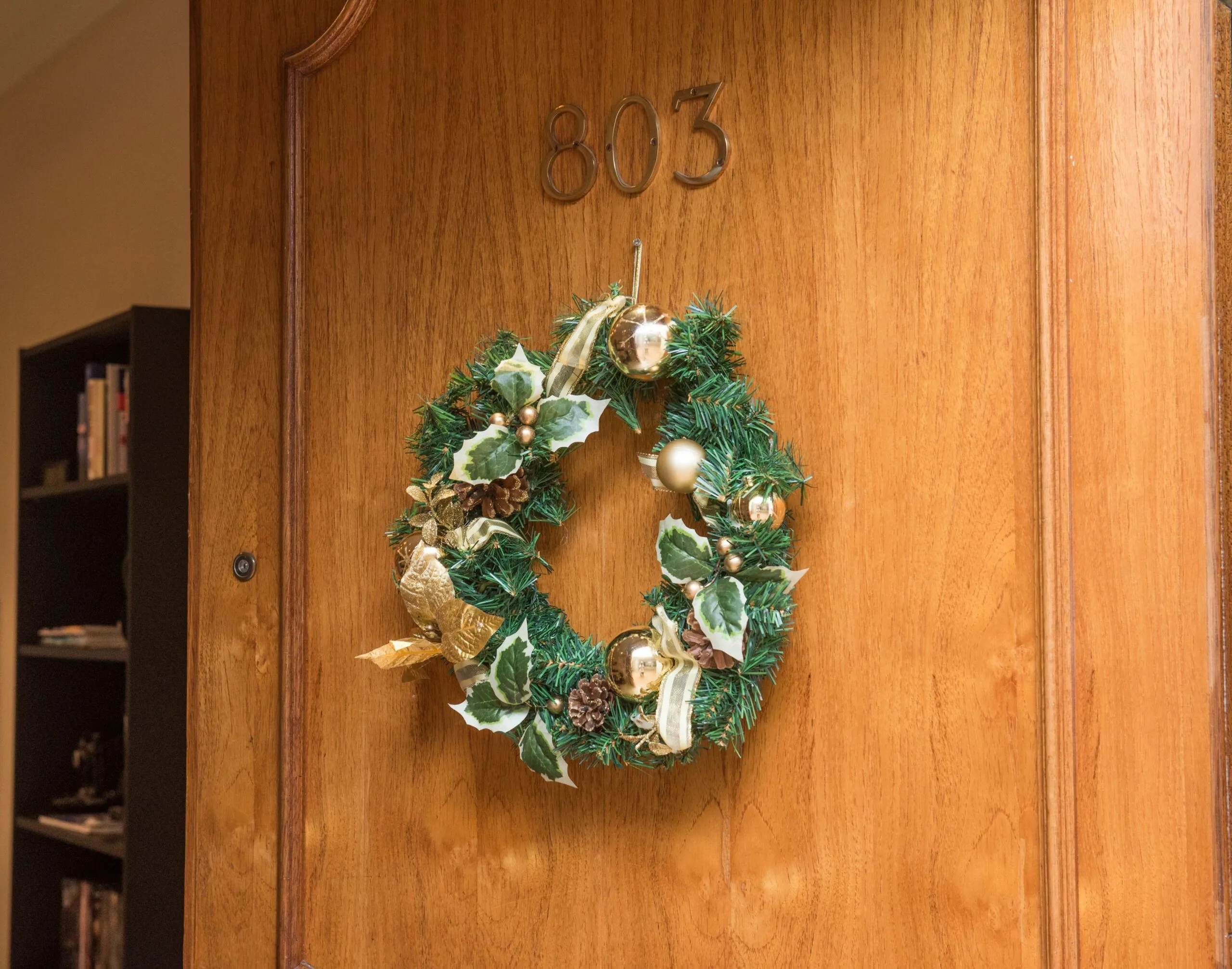 A decorative Christmas wreath adorns a wooden door with room number 803, adding festive charm.
