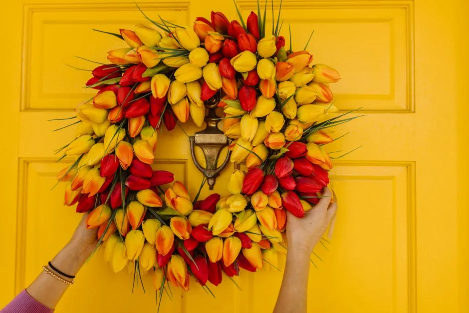 Colorful tulip wreath held by hands on a yellow door, perfect for spring decor.
