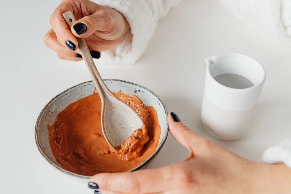 Close-up of hands mixing a natural skincare mask in a ceramic bowl, emphasizing beauty routine.
