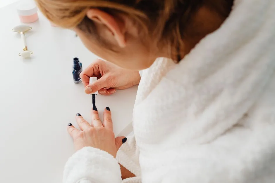 A woman in a bathrobe paints her nails indoors as part of a self-care routine.