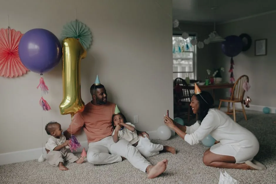 A family celebrating a child's first birthday at home with balloons and party hats.