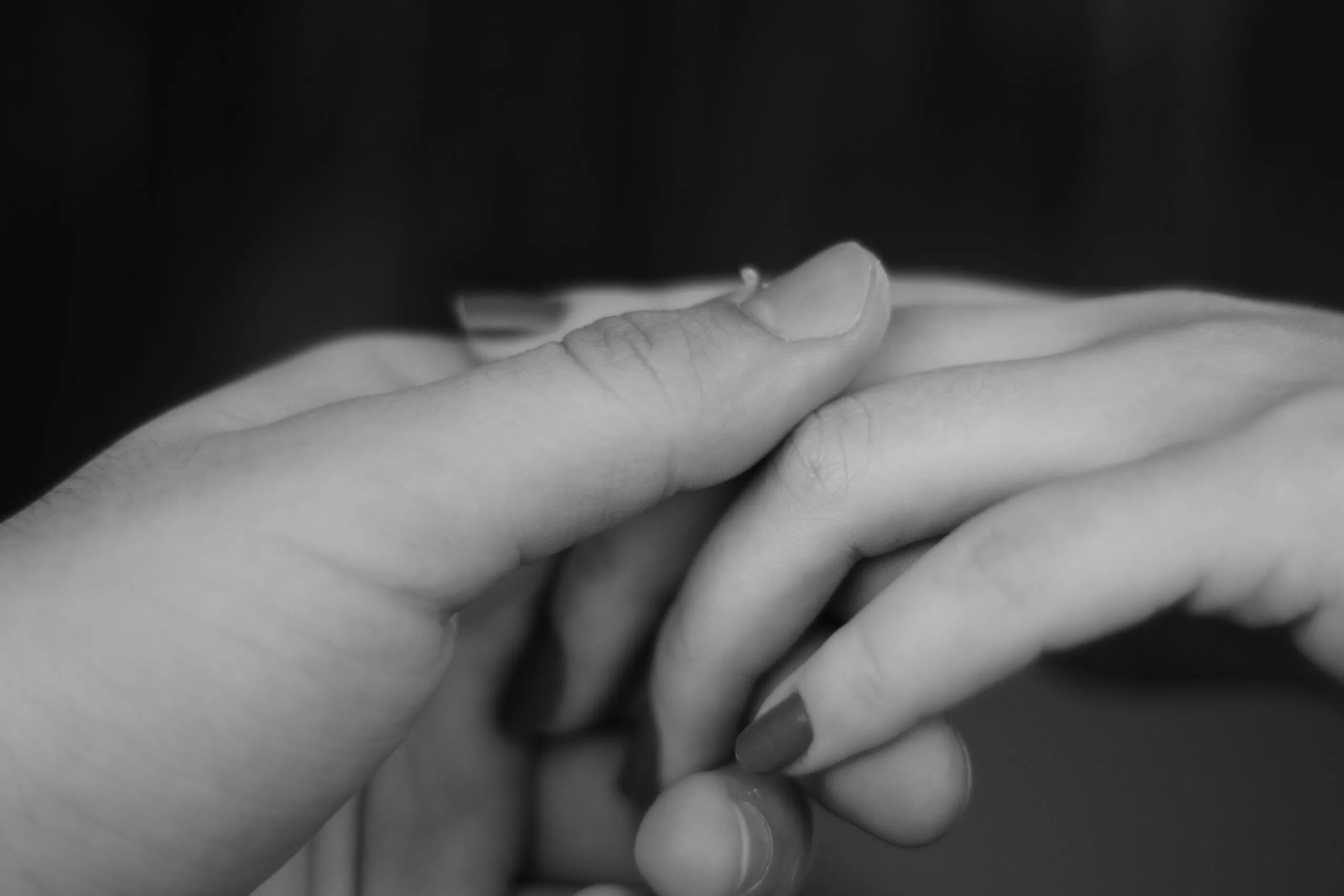 A grayscale close-up of two hands gently touching, conveying connection and emotion.
