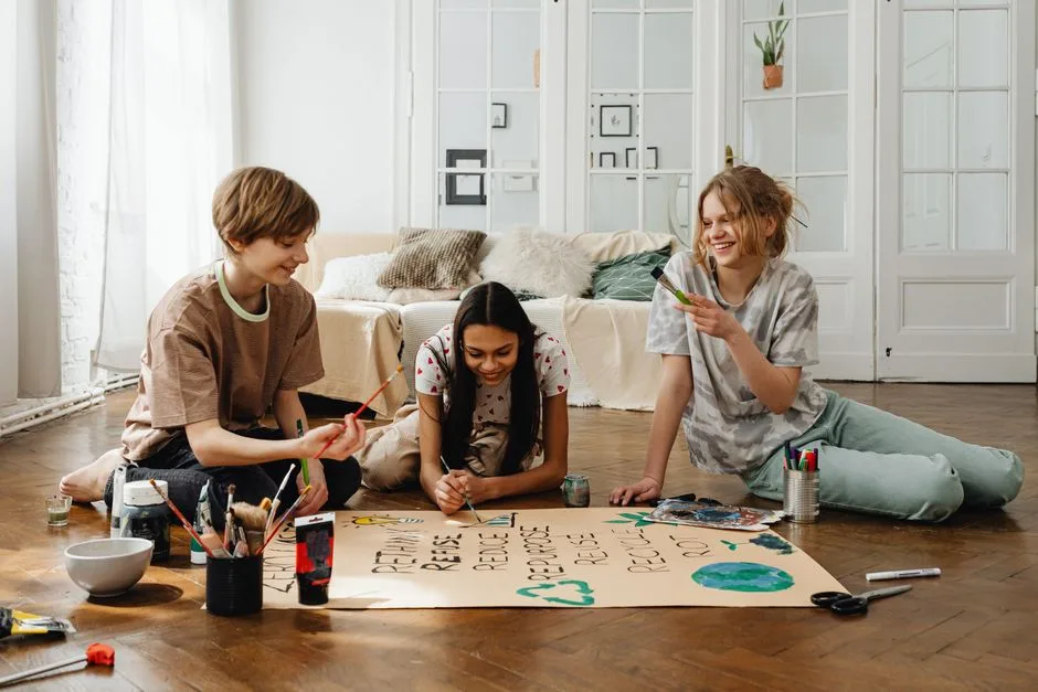 Three teenagers enjoy a fun art project together indoors, surrounded by paint and craft supplies.