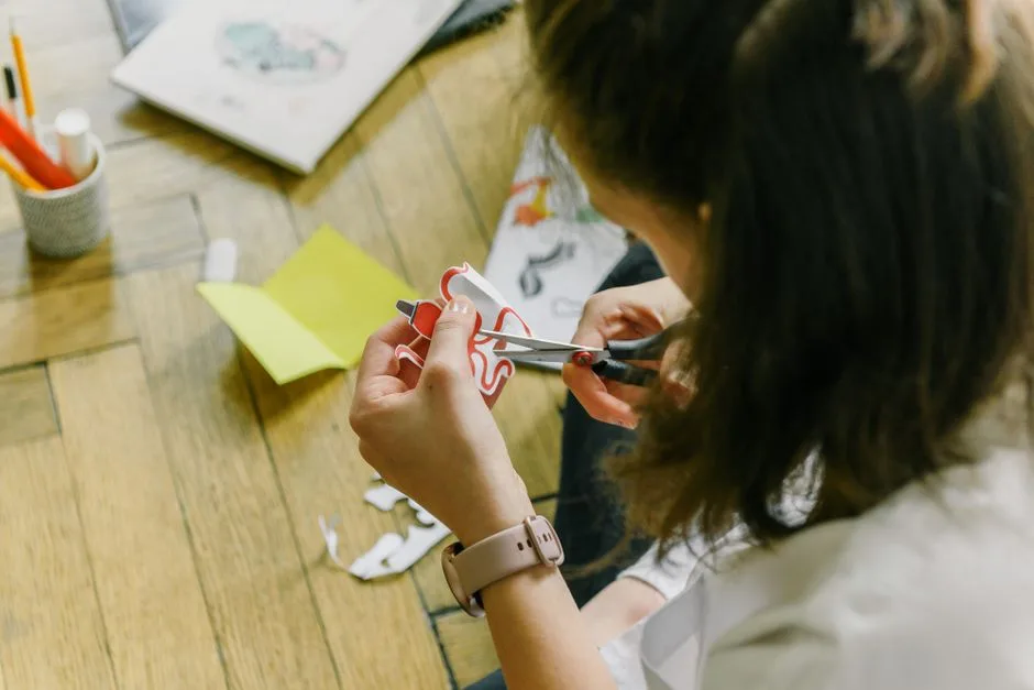 Creative woman using scissors to cut paper designs at home.