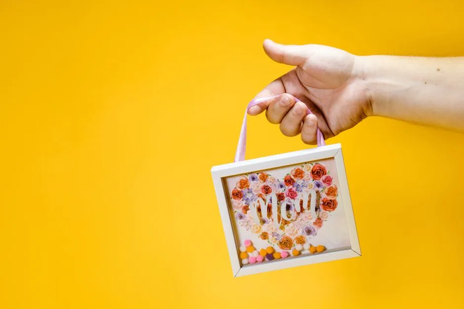 Close-up of a hand holding a floral-themed Mother's Day gift on a vibrant yellow background.