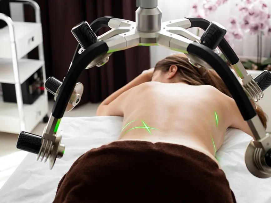 Back view of anonymous female client lying on medical table under lasers of weight loss machine during slimming treatment in clinic