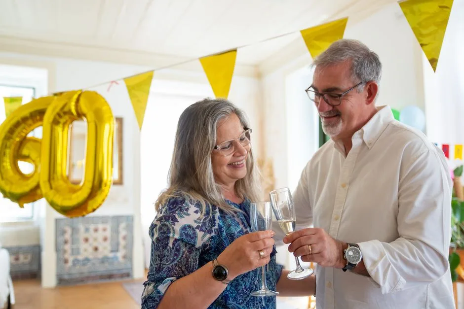Elderly couple toasting at a 60th birthday party with festive decor and champagne.