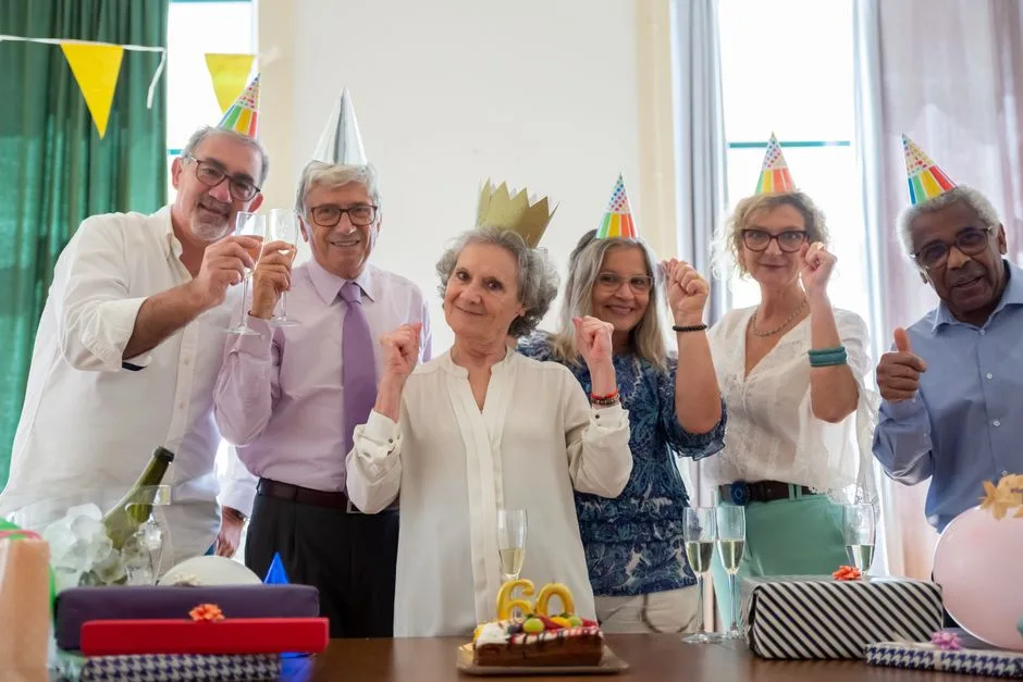 Group of seniors joyfully celebrating a birthday with party hats and cake indoors.