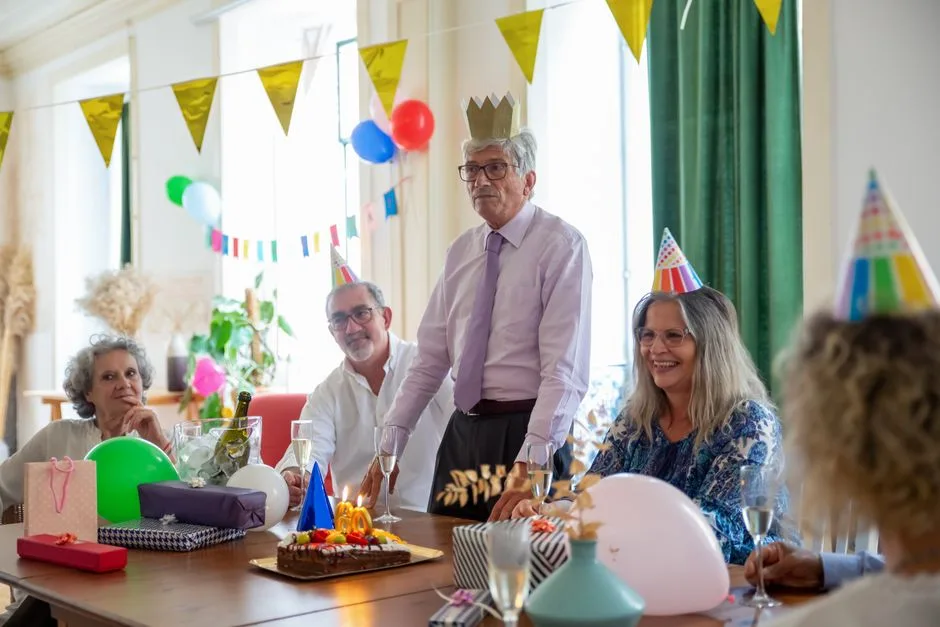 Smiling seniors celebrating a birthday party indoors with decorations and cake.