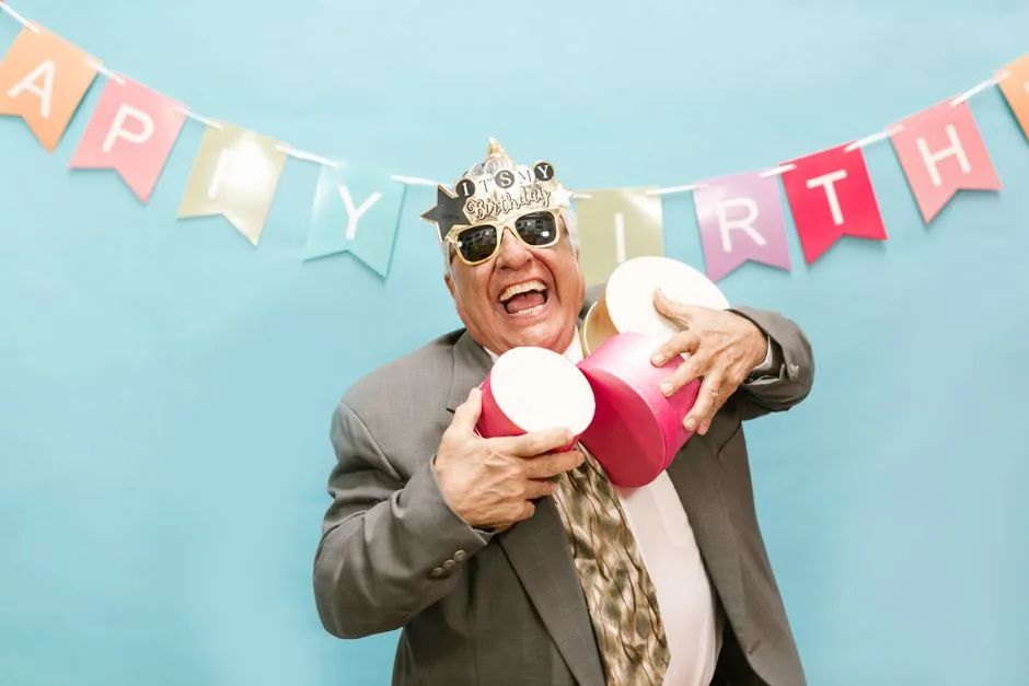 Elderly man joyfully celebrating his birthday with decorations and gifts.