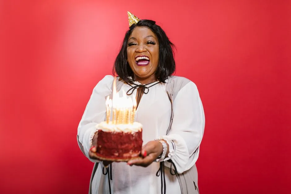 Happy woman celebrating birthday with a cake and candles in a studio setting.