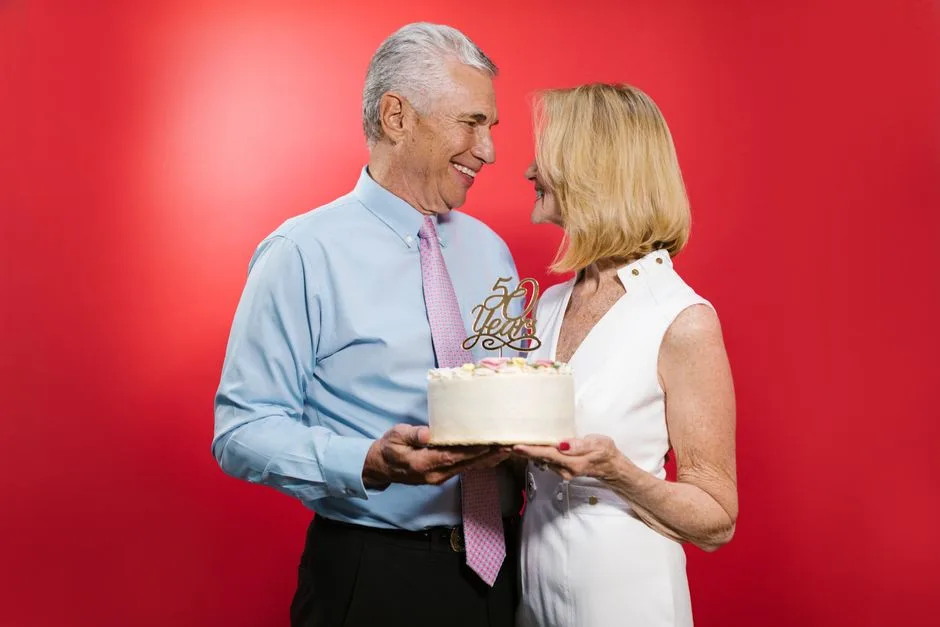Happy senior couple celebrating their 50th anniversary with cake in a studio setting.