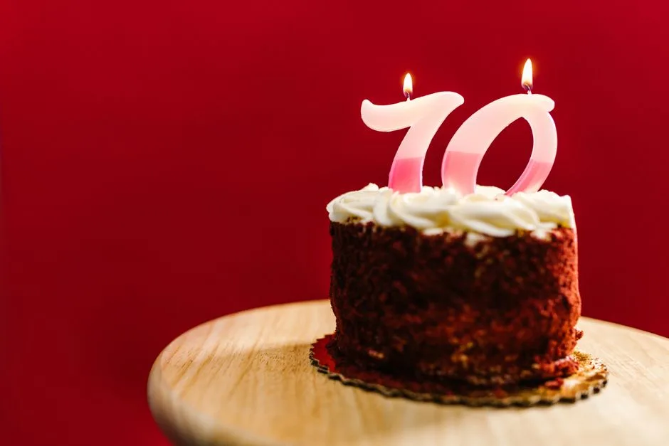 Delicious red velvet cake with number 70 candles on a wooden stand against a red backdrop.