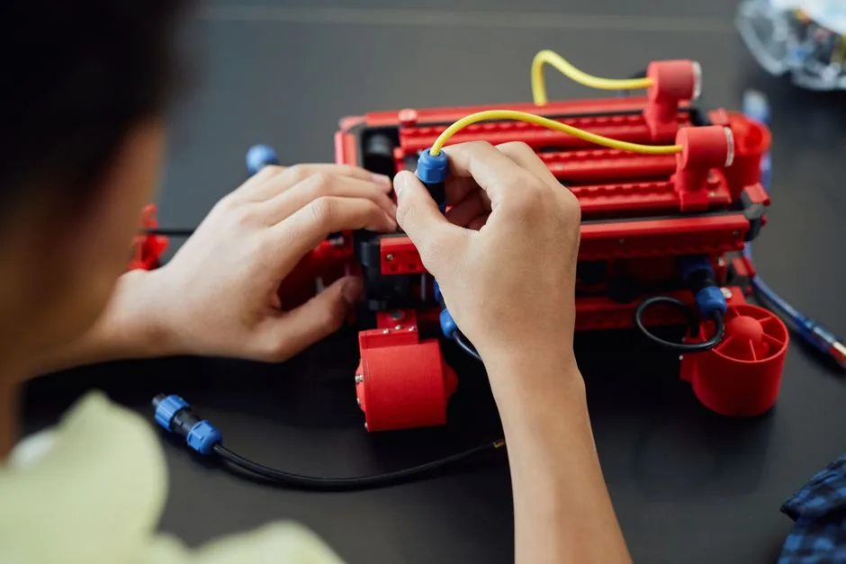 Close-up of hands assembling a robotic project with cables indoors, showcasing technology and electronics.