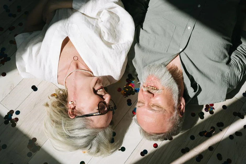 A happy senior couple lying on the floor surrounded by confetti, sharing a joyful moment.