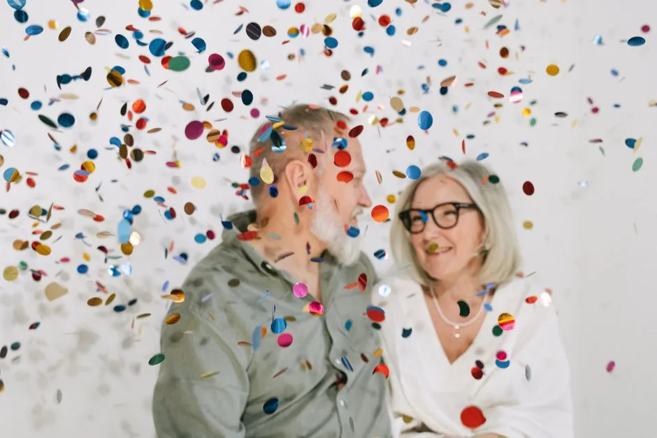 Senior couple enjoying a joyful celebration with colorful confetti indoors.