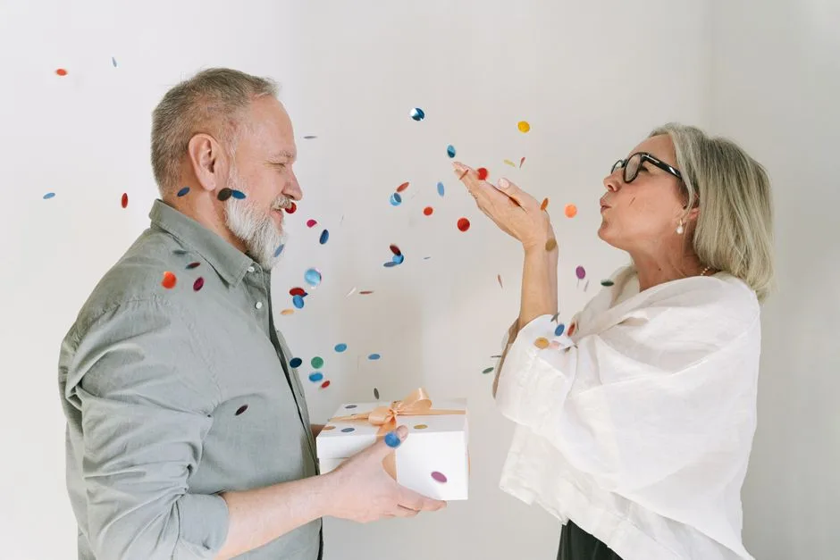 Elderly couple celebrating with confetti and a gift, expressing joy and love.