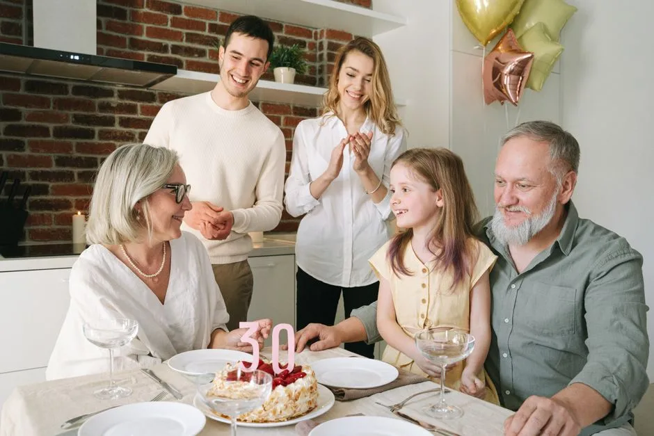 Family with three generations celebrating a 30th anniversary with a cake and balloons indoors.