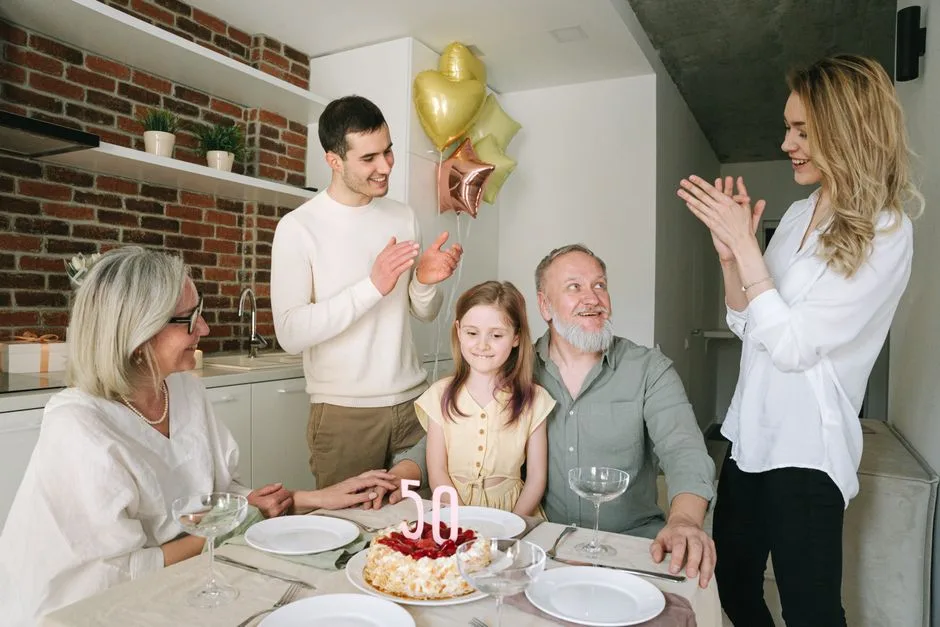 Happy family celebrating a 50th birthday with cake and balloons, enjoying togetherness indoors.