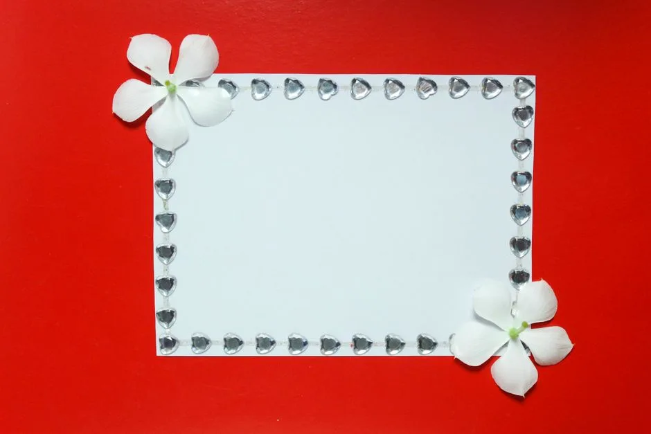 A blank decorative card adorned with white flowers and heart-shaped gems on a red background.