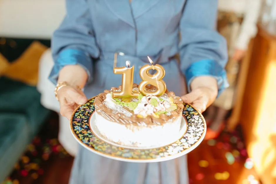 Close-up of hands holding a birthday cake with '18' candles for a celebration.