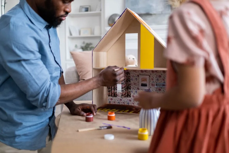 A man and a child painting a dollhouse together, focusing on creativity and craftsmanship.