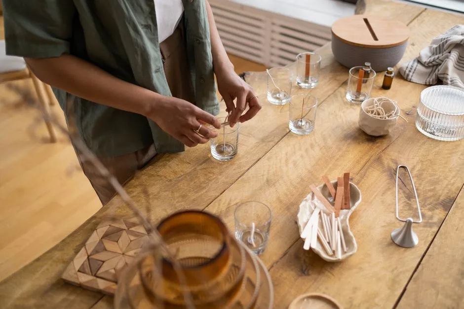 A person crafting candles with natural materials on a wooden table indoors.