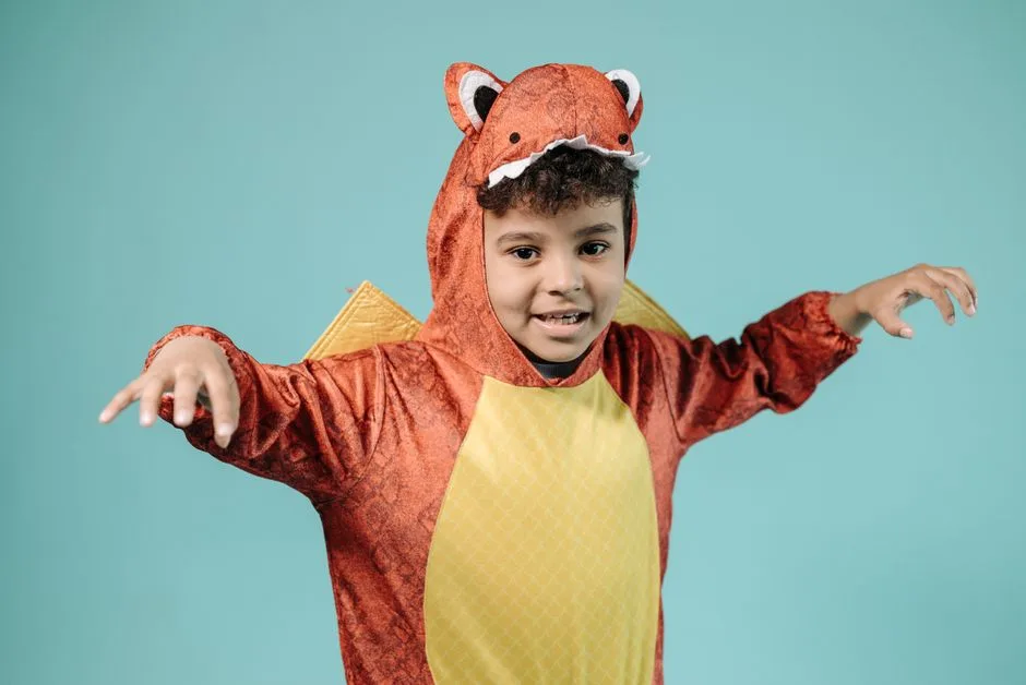 A cheerful child in a dinosaur costume posing against a plain blue backdrop.