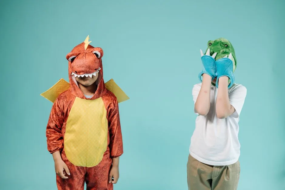 Two children dressed in dinosaur costumes having fun against a turquoise backdrop in a studio setting.
