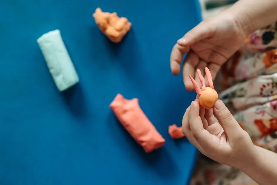Young hands shaping colorful clay into fun figures on a vibrant blue background.