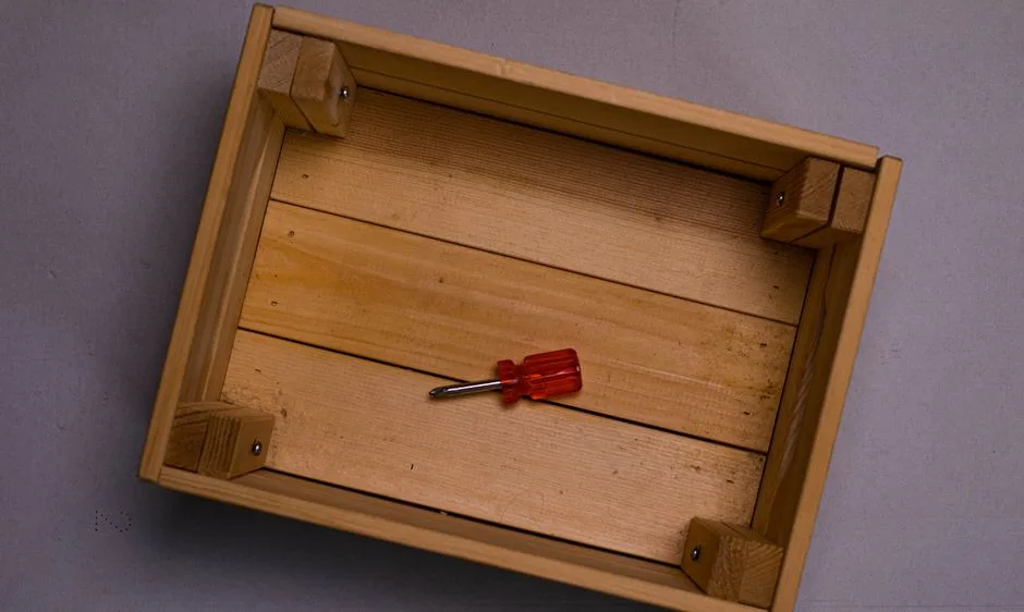 Flat lay of a wooden box with a red screwdriver placed inside on a neutral surface.