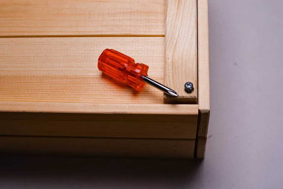 Close-up of an orange screwdriver on a wooden box corner showing precise assembly.