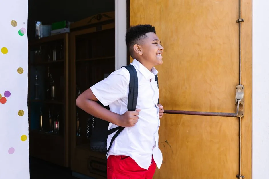 A smiling boy with a backpack entering school, ready for a new academic year.