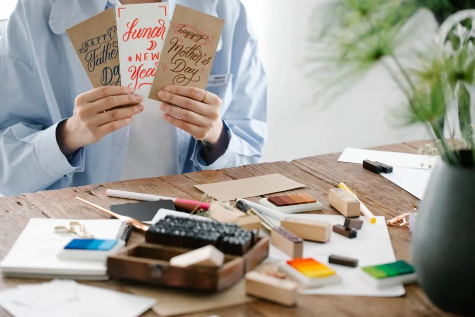 Creative greeting cards held above a messy workspace.