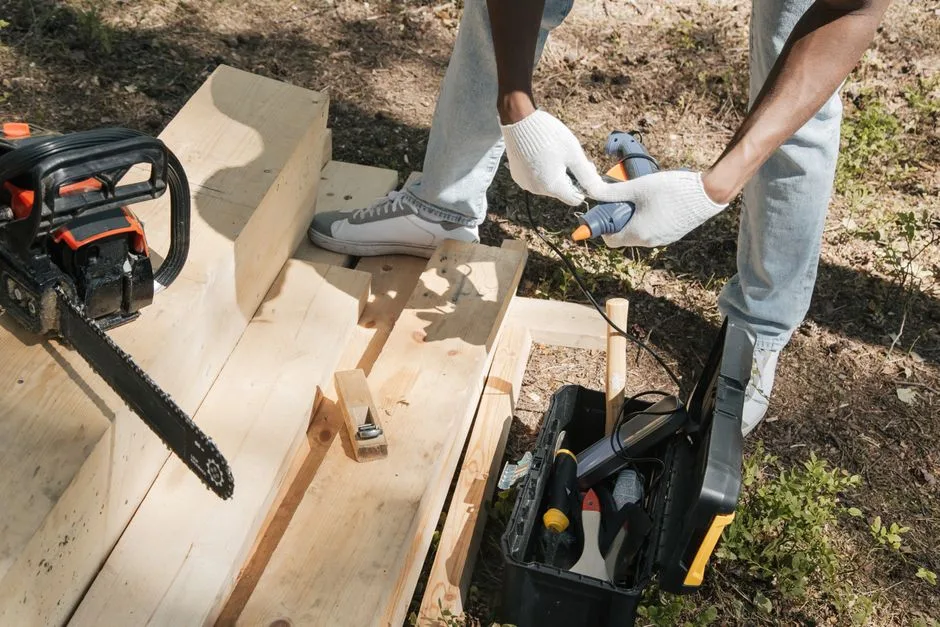 A carpenter using power tools to work on a wooden panel outdoors, showcasing construction and craftsmanship.