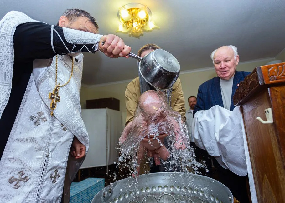 A religious baptism ceremony with a priest pouring water on a baby's head in church.