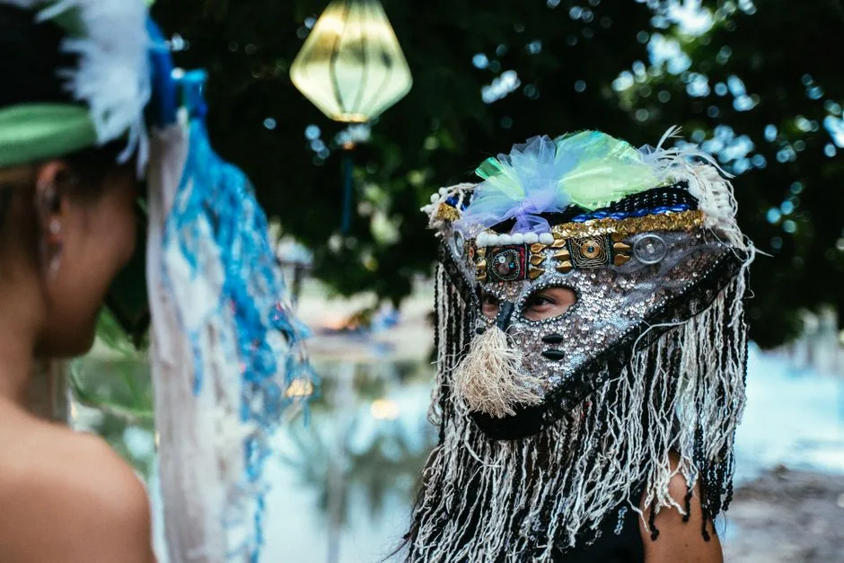 Colorful ethnic celebration with masked individuals under lantern-lit trees.