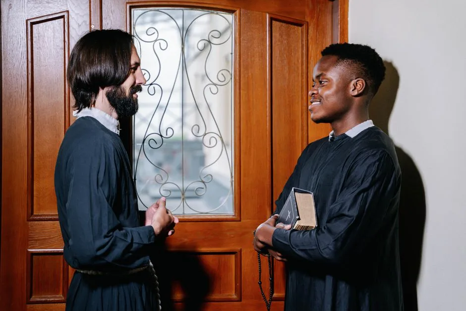 Two priests sharing a friendly discussion indoors, one holding a Bible, enhancing the spiritual atmosphere.