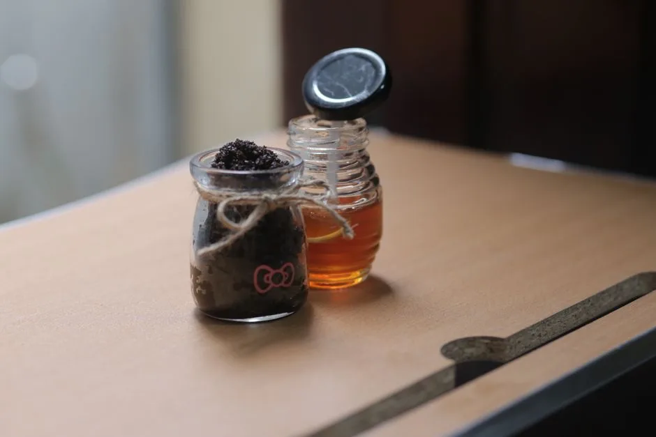 Close-up of glass jars with honey and body scrub, set on a wooden table, showcasing natural skincare ingredients.