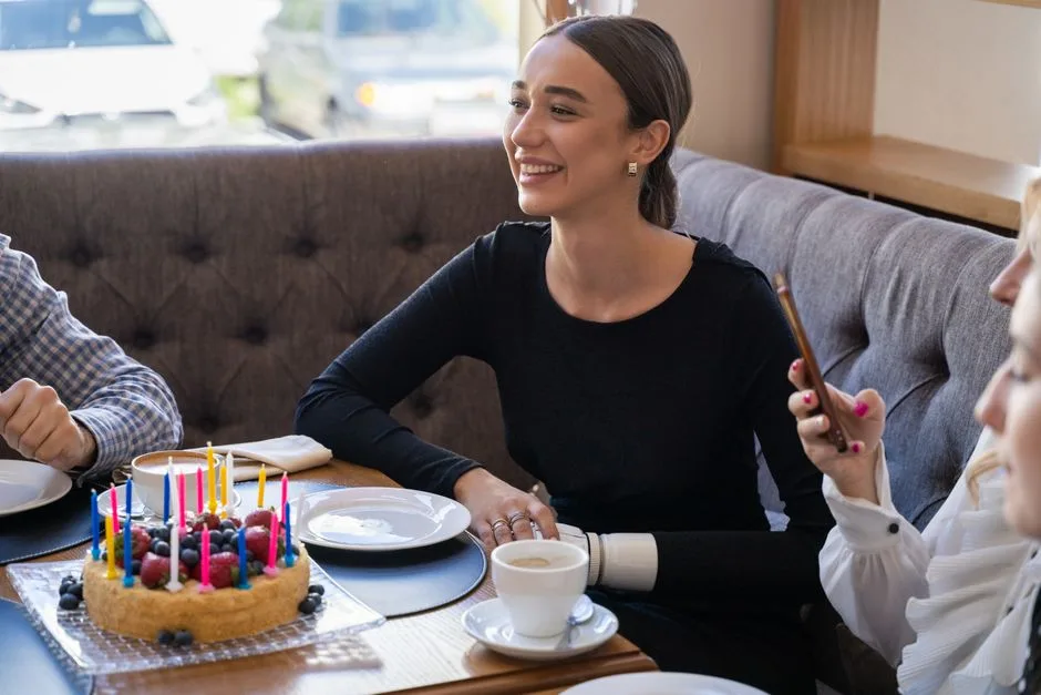 A woman celebrates her birthday with friends, enjoying a cake and coffee in a cozy cafe setting.